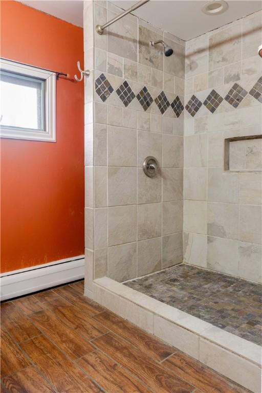 full bathroom featuring a baseboard heating unit, wood finished floors, and a tile shower