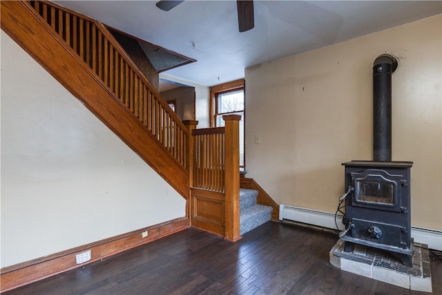 living room with dark wood-style floors, baseboard heating, a wood stove, baseboards, and stairs