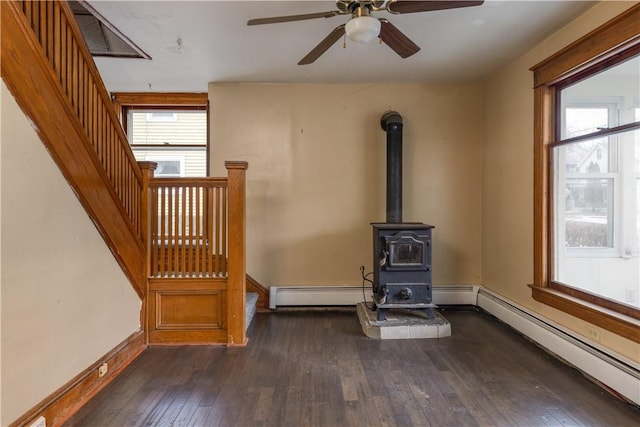 unfurnished living room featuring a baseboard heating unit, plenty of natural light, dark wood-style floors, and a wood stove