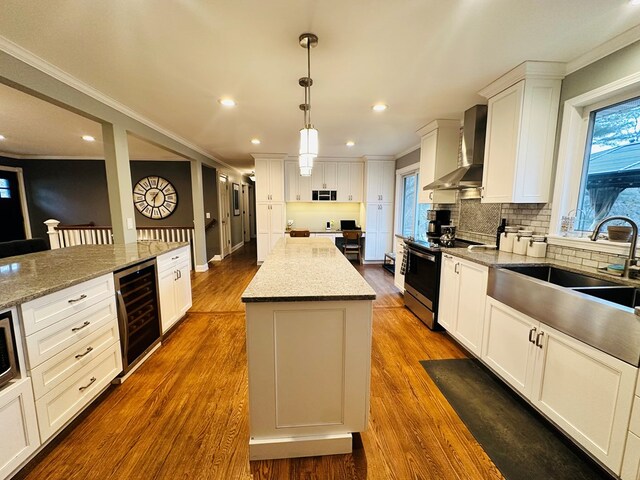 kitchen featuring white cabinets, wine cooler, a center island, electric range, and wall chimney range hood