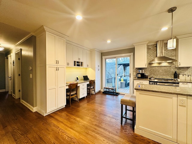 kitchen featuring stove, wall chimney range hood, dark stone counters, and white cabinets