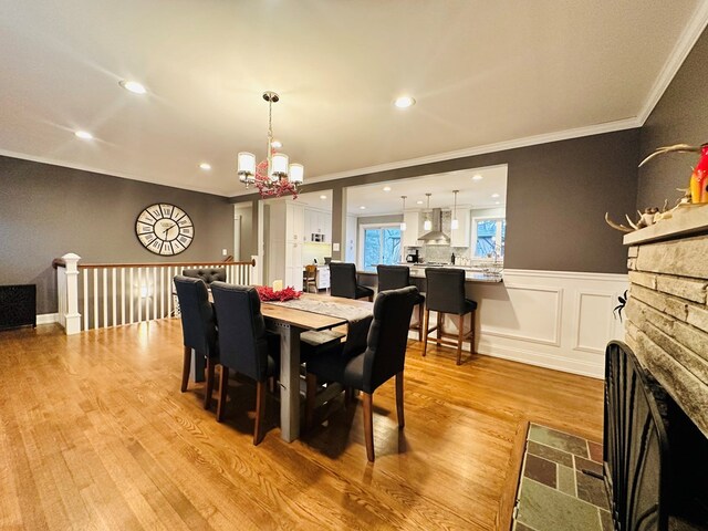 dining area featuring an inviting chandelier, a stone fireplace, light hardwood / wood-style floors, and crown molding