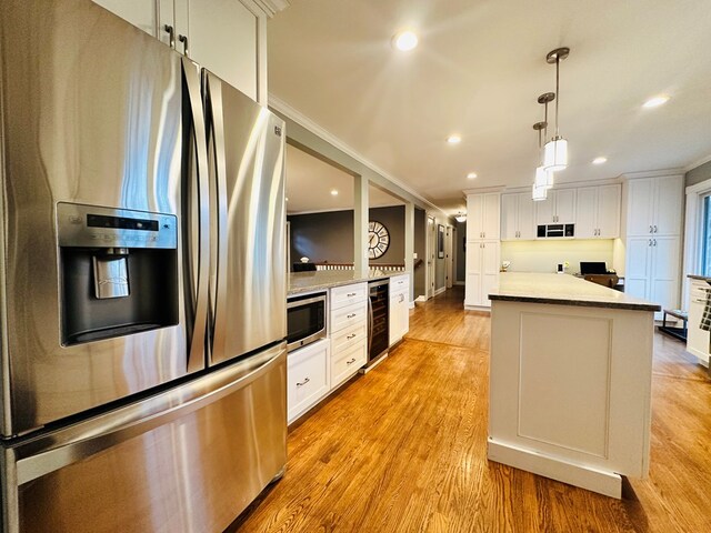 kitchen featuring appliances with stainless steel finishes, decorative light fixtures, white cabinetry, wine cooler, and a center island