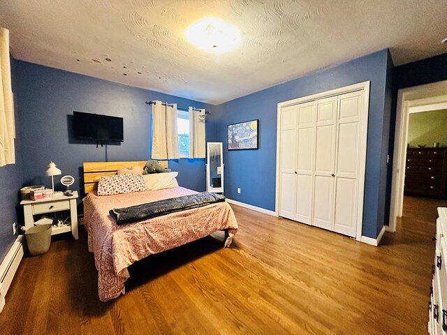 bedroom featuring baseboard heating, hardwood / wood-style floors, a textured ceiling, and a closet