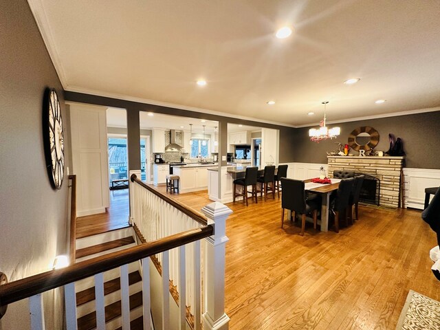 dining space featuring a notable chandelier, crown molding, a stone fireplace, and light hardwood / wood-style floors