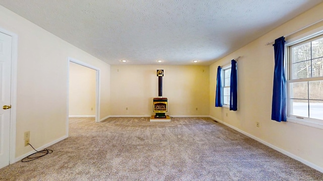 11827 Lando Ln, Corning, NY 14830 - empty room featuring a wood stove, a textured ceiling, carpet, and baseboards