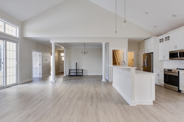 kitchen with ornate columns, appliances with stainless steel finishes, a kitchen island with sink, and pendant lighting