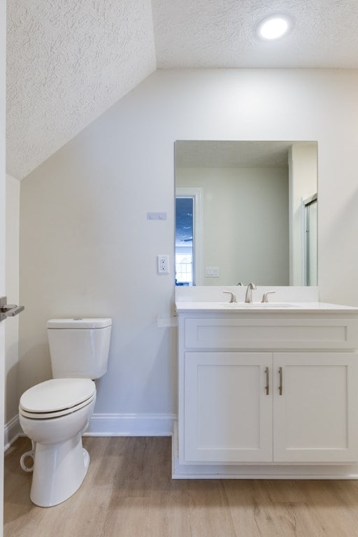 bathroom featuring lofted ceiling, toilet, wood-type flooring, a textured ceiling, and vanity