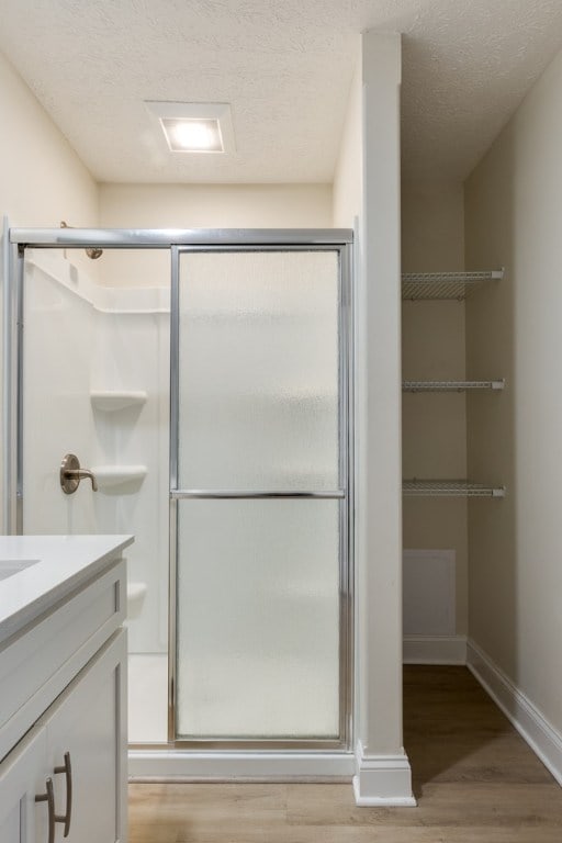 bathroom featuring a shower with door, wood-type flooring, vanity, and a textured ceiling