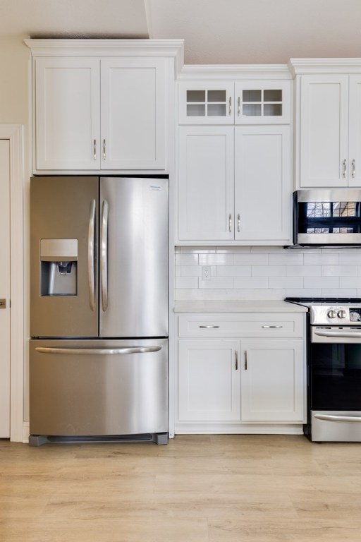 kitchen featuring decorative backsplash, light hardwood / wood-style flooring, white cabinets, and appliances with stainless steel finishes