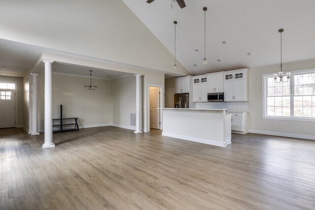 unfurnished living room featuring ornate columns, high vaulted ceiling, ceiling fan with notable chandelier, and light wood-type flooring