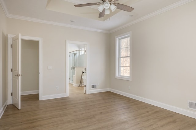 unfurnished bedroom with a tray ceiling, light hardwood / wood-style flooring, ornamental molding, and ensuite bathroom