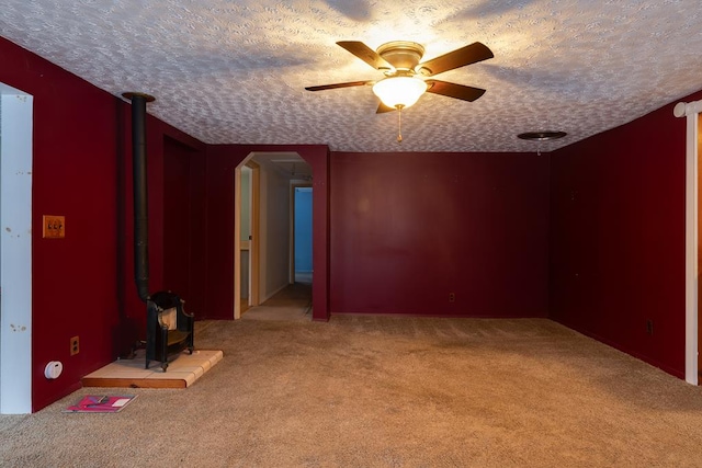 empty room with ceiling fan, light carpet, a textured ceiling, and a wood stove