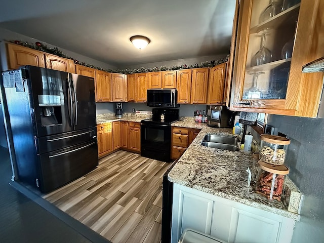 kitchen with light stone counters, light hardwood / wood-style floors, sink, and black appliances