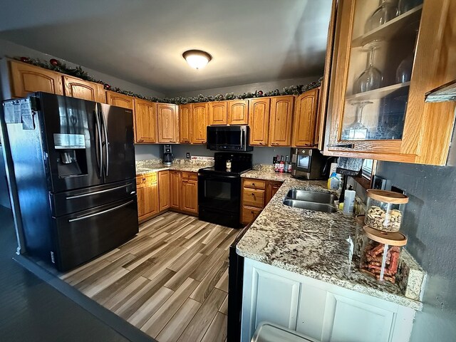 kitchen with glass insert cabinets, brown cabinets, a sink, and black appliances