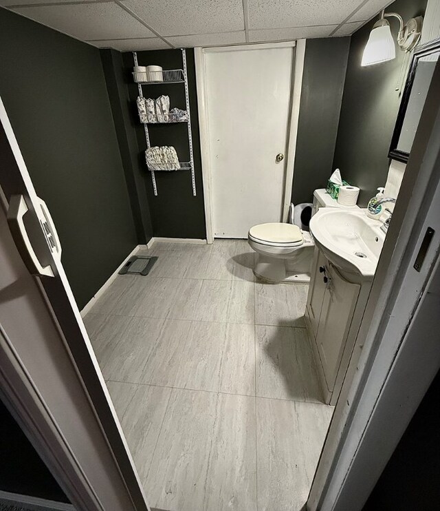 bathroom featuring vanity, toilet, and a drop ceiling