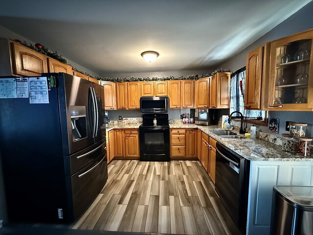 kitchen with glass insert cabinets, brown cabinetry, a sink, and black appliances