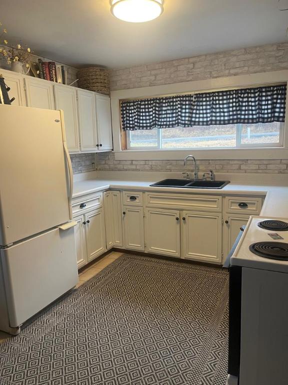 kitchen with sink, light tile patterned floors, white cabinetry, electric range oven, and white fridge