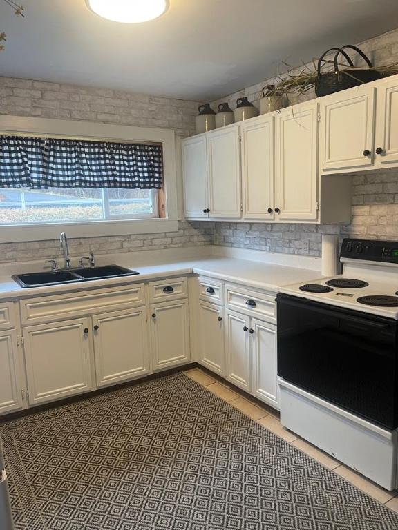 kitchen featuring backsplash, white electric range oven, sink, and white cabinets