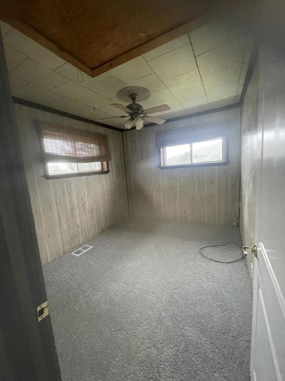 basement with carpet floors, wooden walls, and ceiling fan