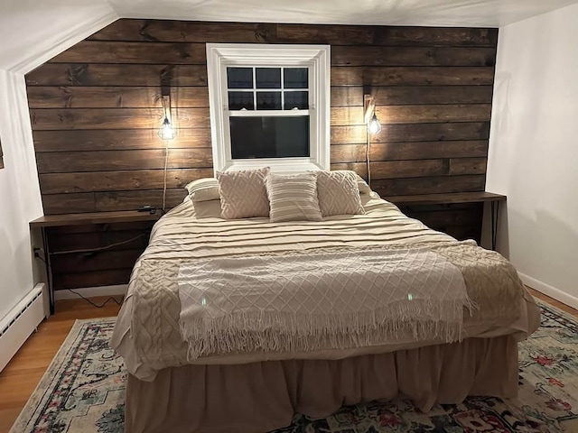 bedroom with a baseboard heating unit, wood walls, and light wood-type flooring