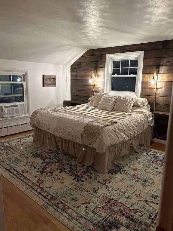 bedroom with lofted ceiling, cooling unit, a baseboard radiator, wooden walls, and hardwood / wood-style flooring