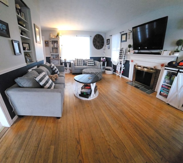 living room featuring wood-type flooring, a fireplace, and built in features