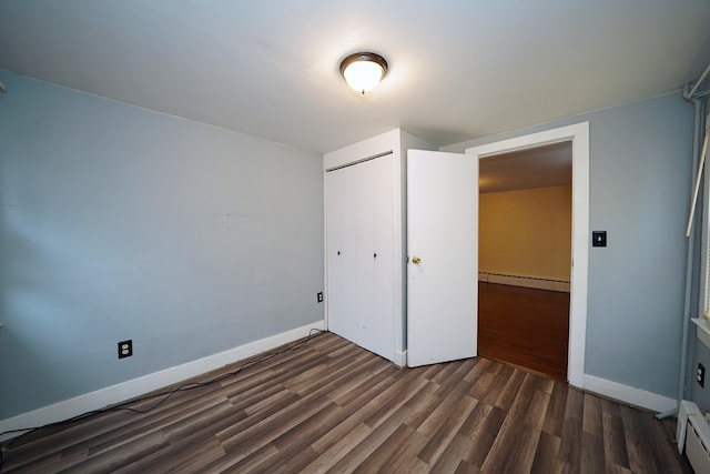 unfurnished bedroom with a baseboard heating unit, dark hardwood / wood-style floors, and a closet