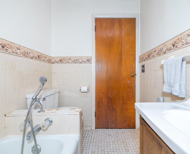 bathroom with tile walls, a bathtub, tile patterned flooring, vanity, and toilet