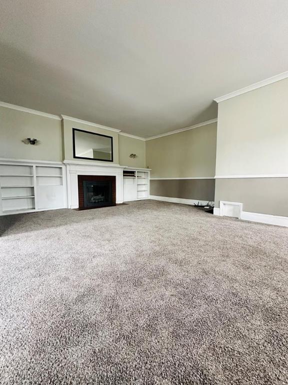 unfurnished living room featuring ornamental molding and carpet floors