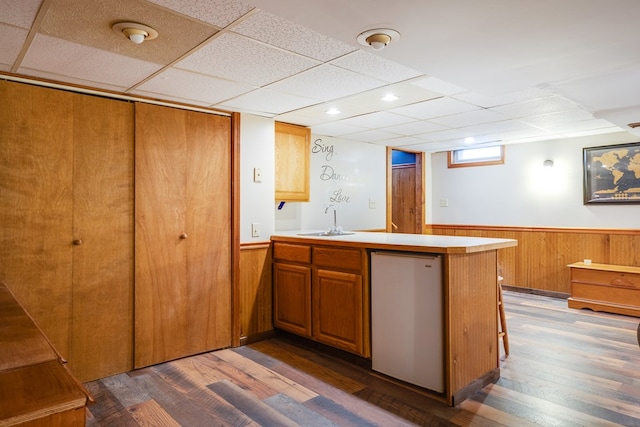 kitchen with dishwashing machine, sink, wooden walls, dark hardwood / wood-style flooring, and kitchen peninsula