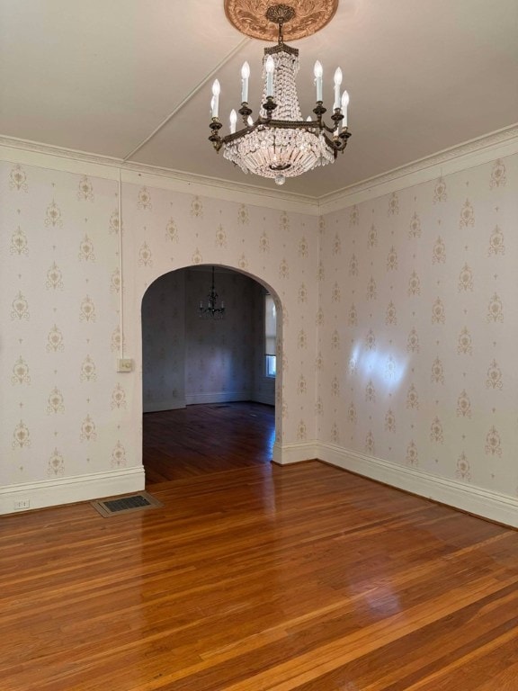 empty room with ornamental molding, hardwood / wood-style floors, and a notable chandelier