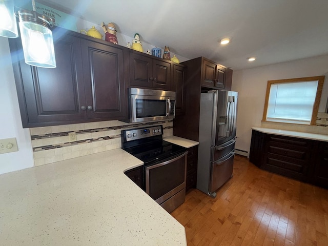 kitchen featuring hanging light fixtures, stainless steel appliances, light stone counters, wood-type flooring, and decorative backsplash