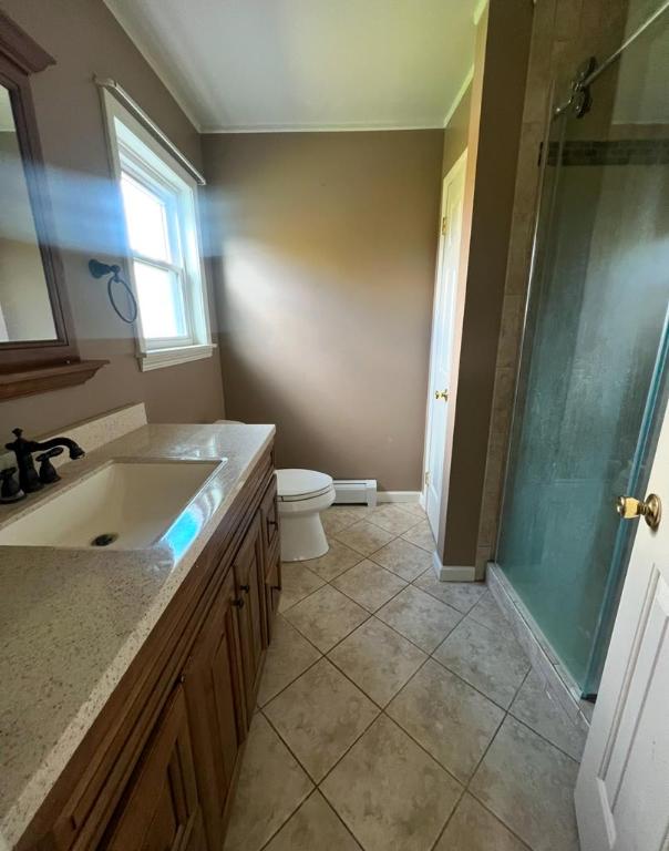 bathroom with toilet, tile patterned floors, vanity, and tiled shower