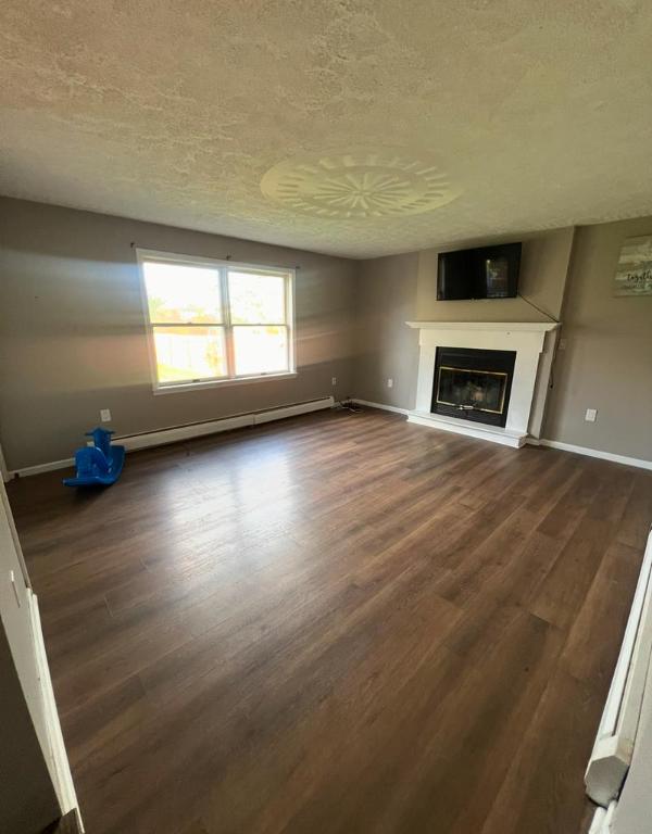 unfurnished living room with baseboard heating, dark hardwood / wood-style floors, and a textured ceiling