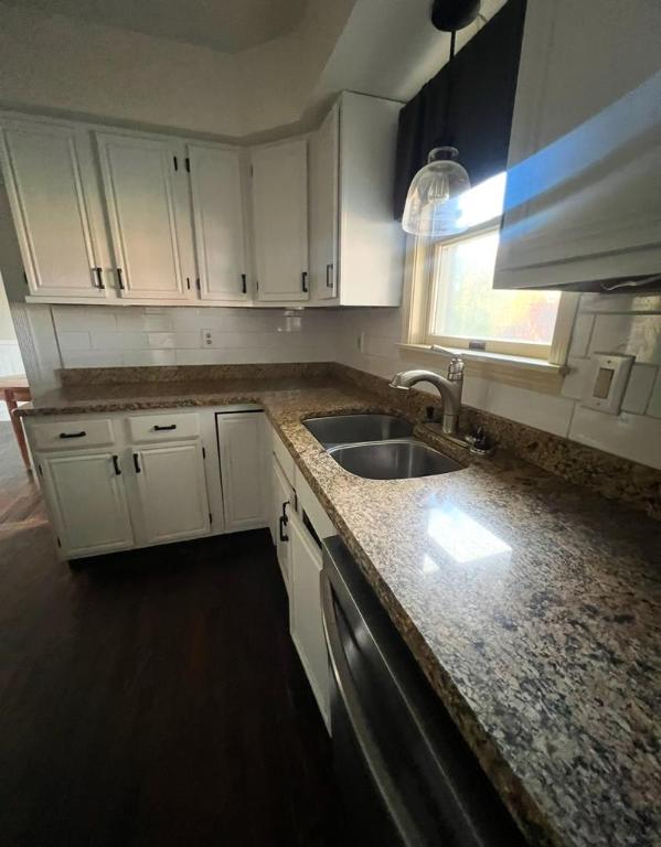 kitchen with white cabinetry, dishwasher, sink, hanging light fixtures, and light stone countertops