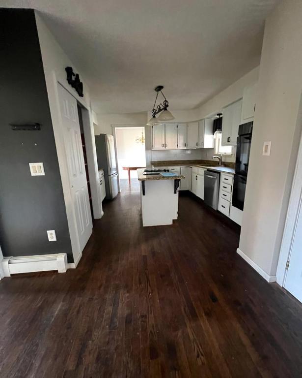 kitchen with dark wood-type flooring, a center island, hanging light fixtures, appliances with stainless steel finishes, and white cabinets