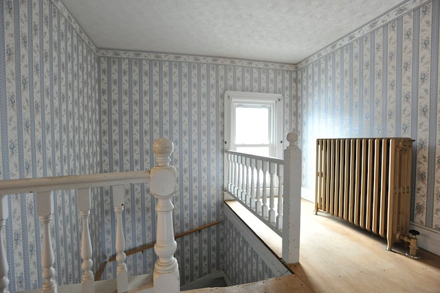 stairway featuring hardwood / wood-style flooring, radiator heating unit, and a textured ceiling