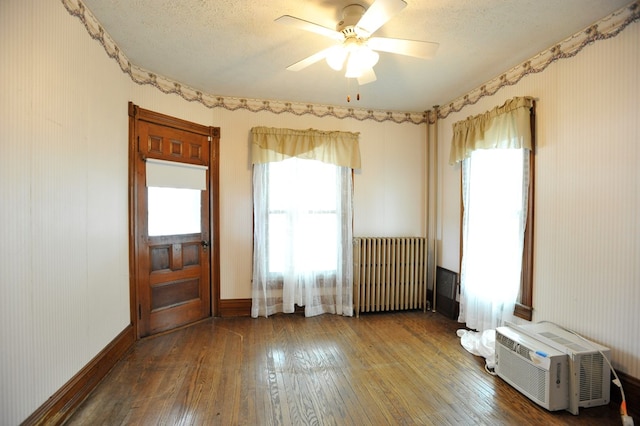 spare room featuring hardwood / wood-style flooring, ceiling fan, radiator heating unit, a wall mounted AC, and a textured ceiling