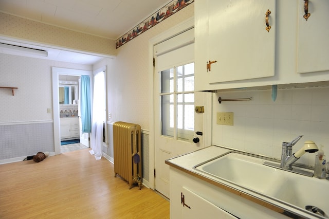 kitchen with light hardwood / wood-style flooring, sink, radiator heating unit, and white cabinets