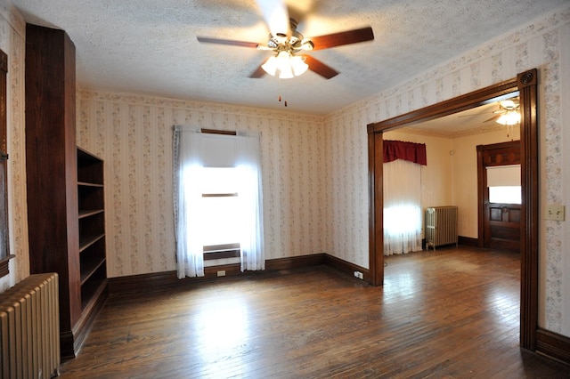 empty room with dark hardwood / wood-style floors, radiator, a wealth of natural light, and a textured ceiling