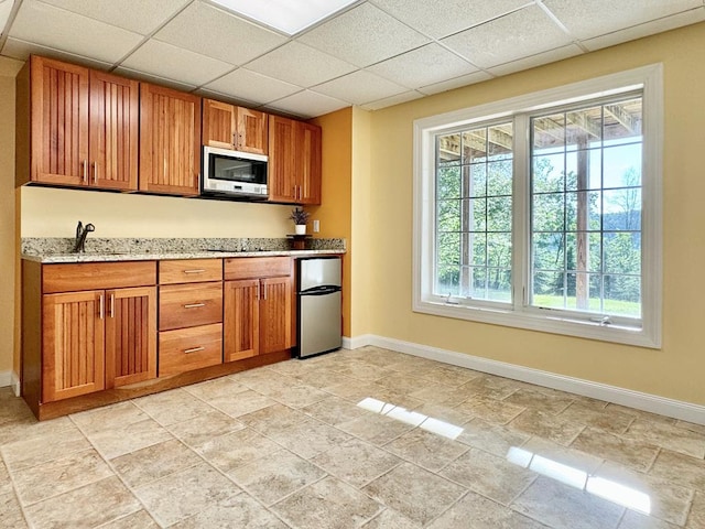 kitchen with sink, a paneled ceiling, light stone countertops, and appliances with stainless steel finishes