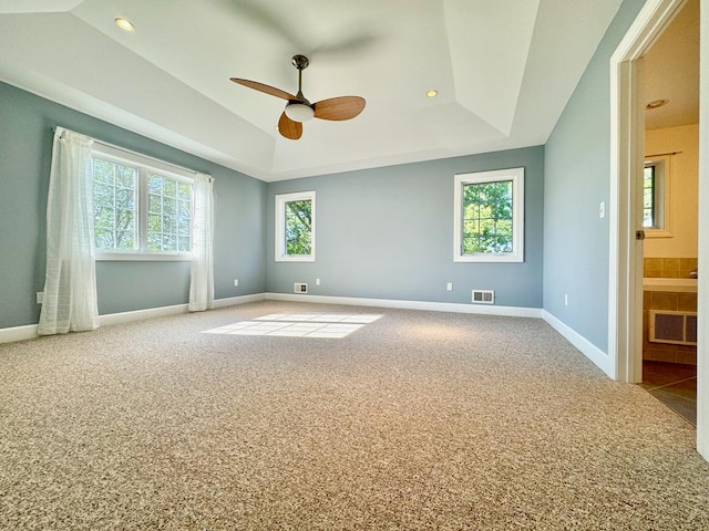 carpeted spare room with ceiling fan, a raised ceiling, and a healthy amount of sunlight