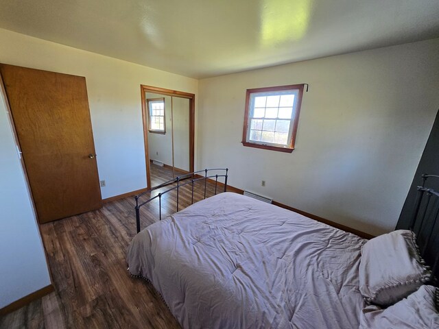 bedroom featuring dark hardwood / wood-style flooring, a baseboard heating unit, and a closet