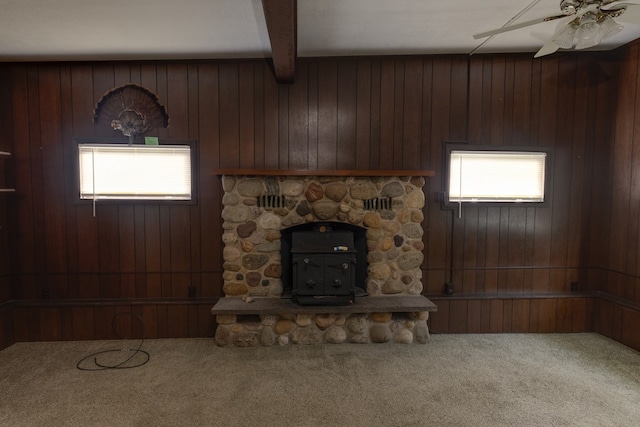 unfurnished living room with a wood stove, wooden walls, carpet floors, ceiling fan, and beam ceiling