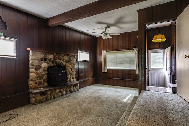 unfurnished living room featuring a wood stove, a textured ceiling, beam ceiling, and carpet flooring