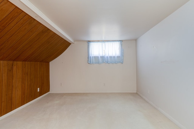 bonus room with vaulted ceiling, light carpet, and wood walls