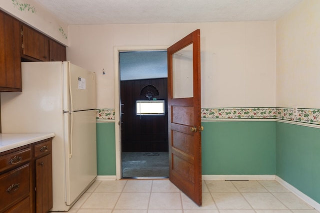 kitchen with white refrigerator, light tile patterned flooring, dark brown cabinets, and a textured ceiling