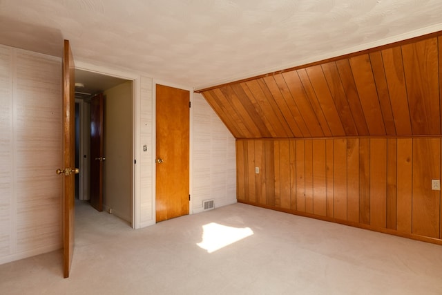 additional living space featuring lofted ceiling, light colored carpet, and wood walls