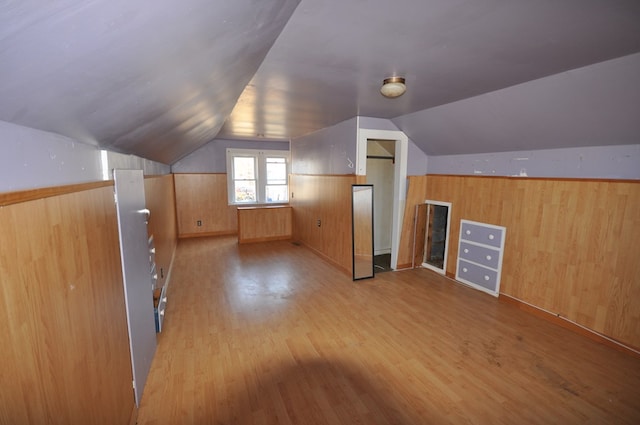 additional living space featuring light hardwood / wood-style flooring, vaulted ceiling, and wood walls